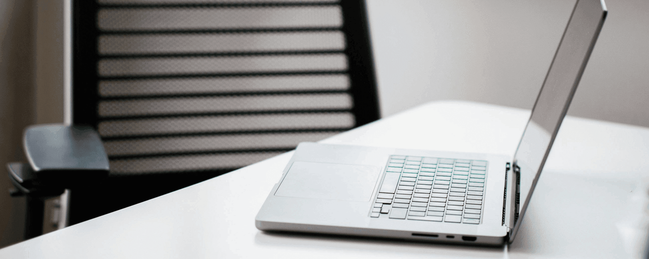 empty desk chair facing an open laptop on table.